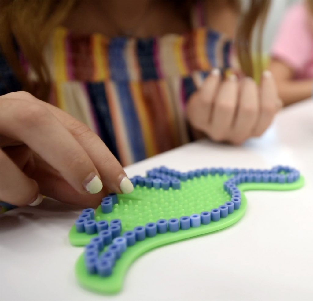 Girl placing colored beads on a pegboard shaped like a dinosaur