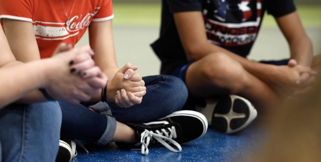Photo of people sitting cross-legged, with hands folded in prayer.
