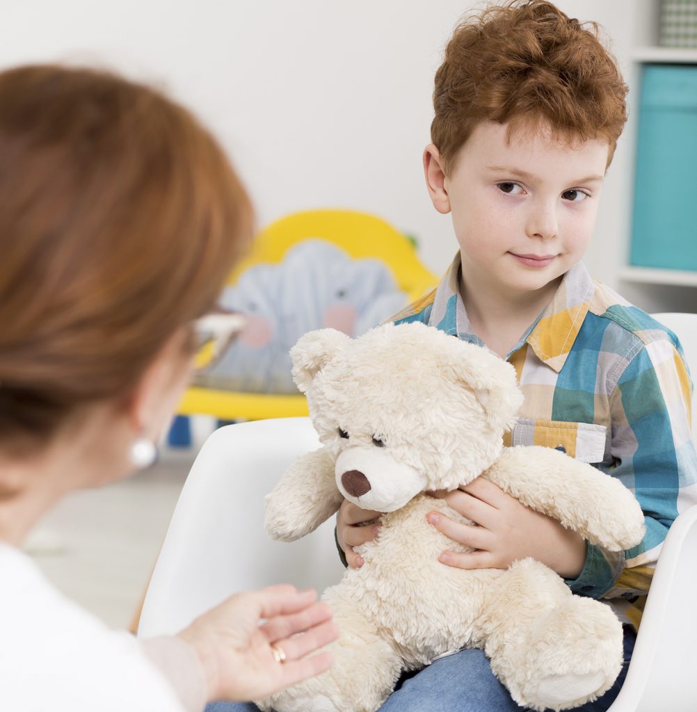 Photo of a young boy sitting in a chair, holding a stuffed toy teddy bear