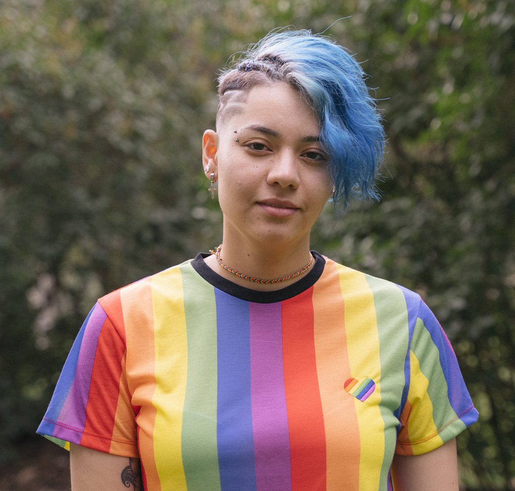 Young woman with blue hair wearing a rainbow-striped T-shirt