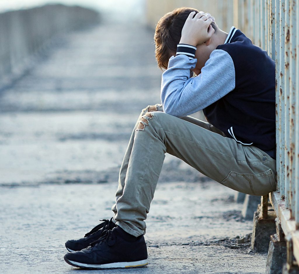 Photo of a sad boy sitting on a bridge