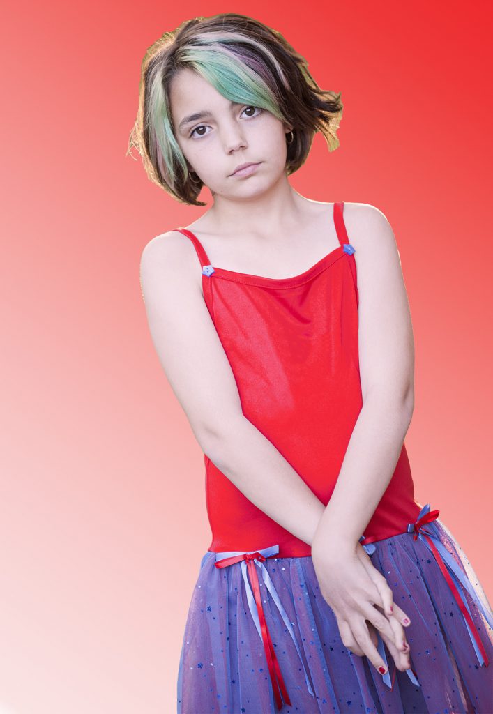 Photo of a girl with a green stripe in her hair, wearing a skirted dancing outfit.