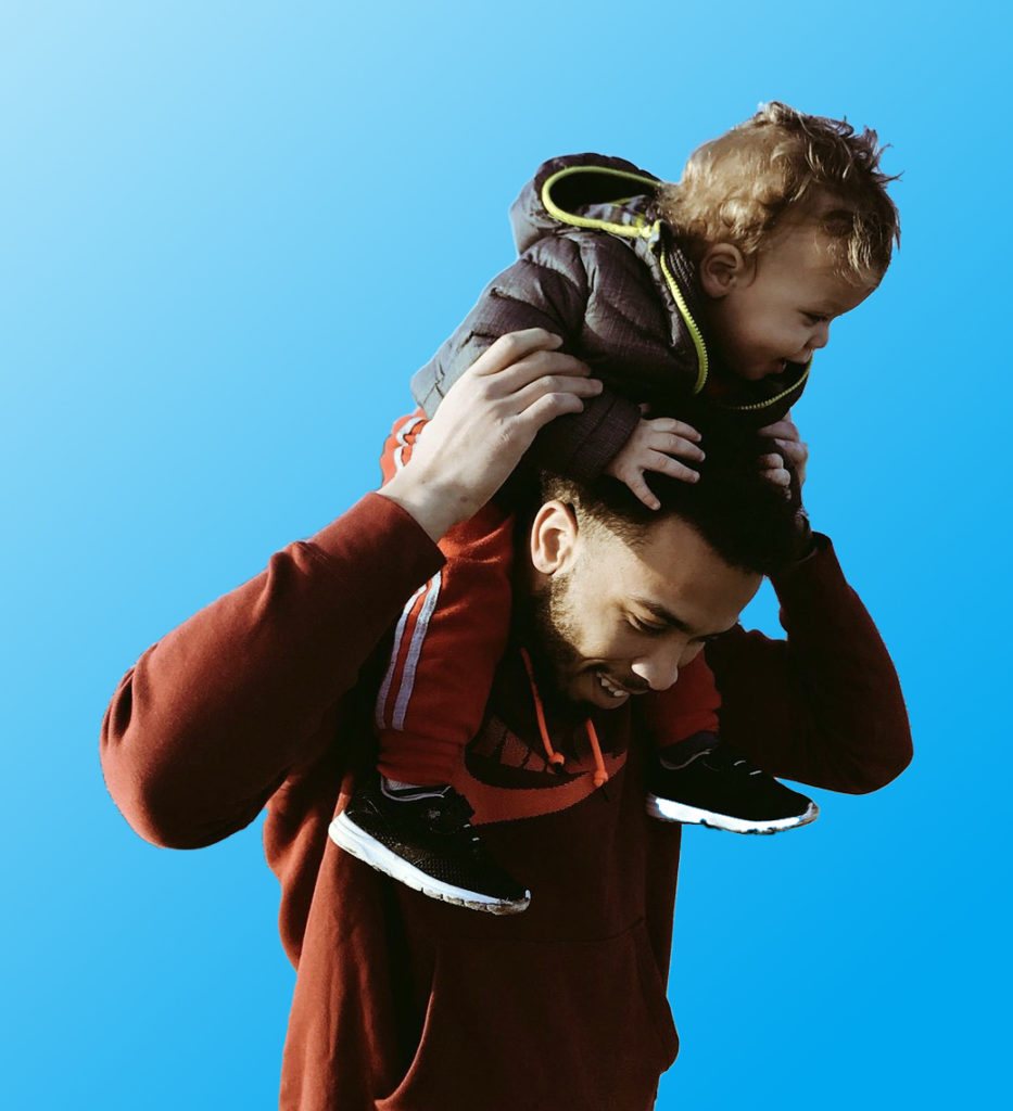 Photo of a father carrying a child on his shoulders.